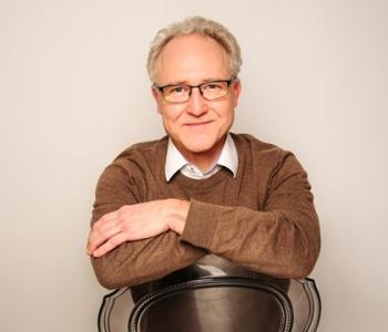 Andreas Roß, sitzend, in braunem Pullover und mit Brille
